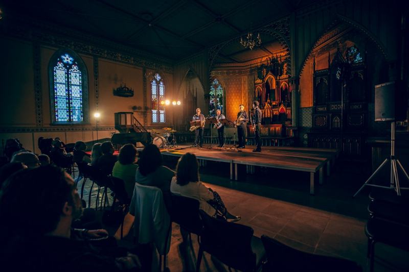 Vista ampla do concerto numa igreja histórica com vitrais e plateia